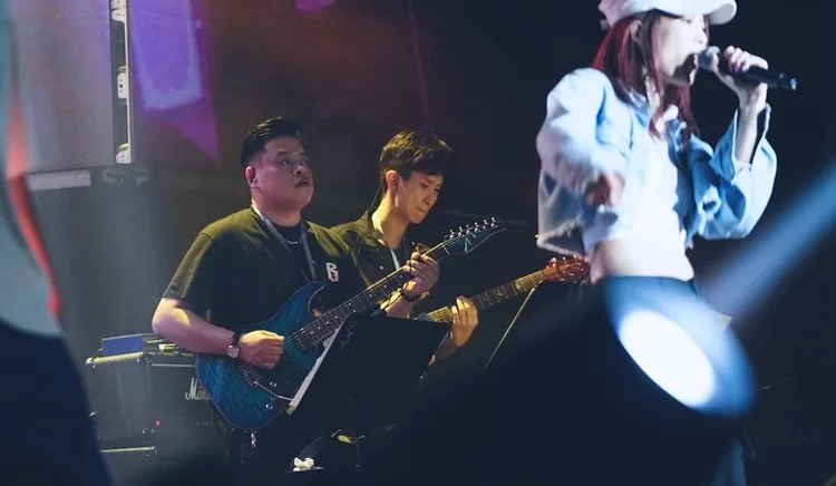 Two electric guitarists accompanying a vocalist under stage lighting