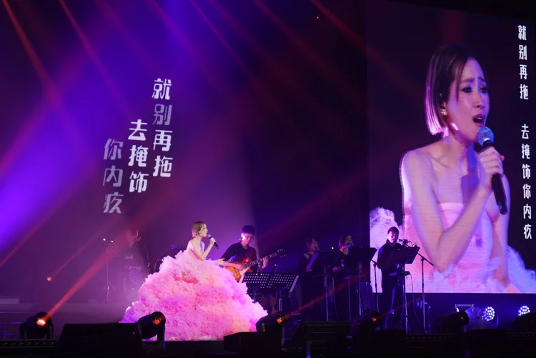 Singer in a pink dress performing with a live band on a large stage