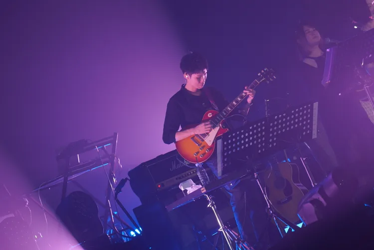 Guitarist playing a sunburst electric guitar under purple stage lighting