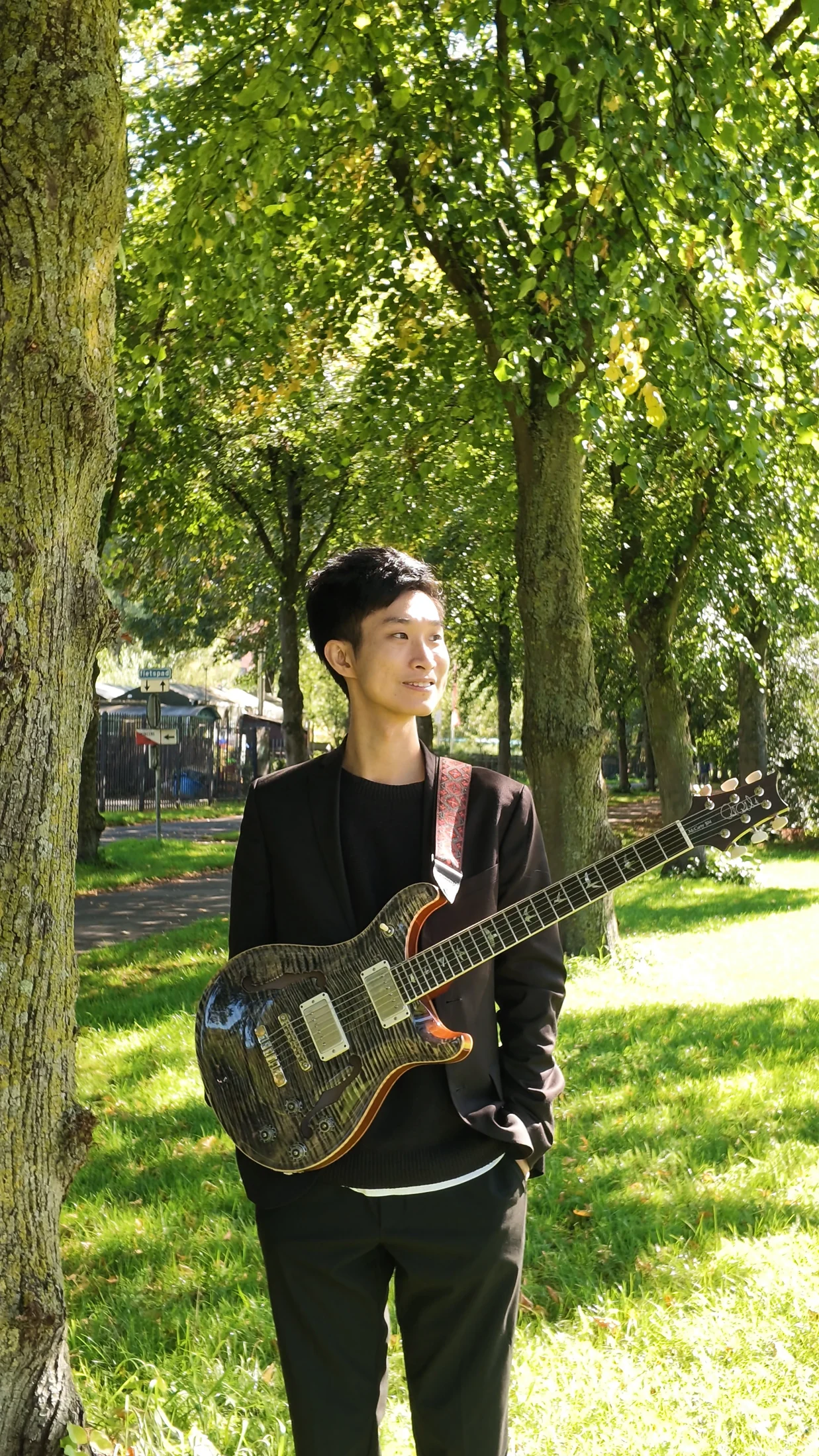 Jiasheng Hu holding an electric guitar under the trees