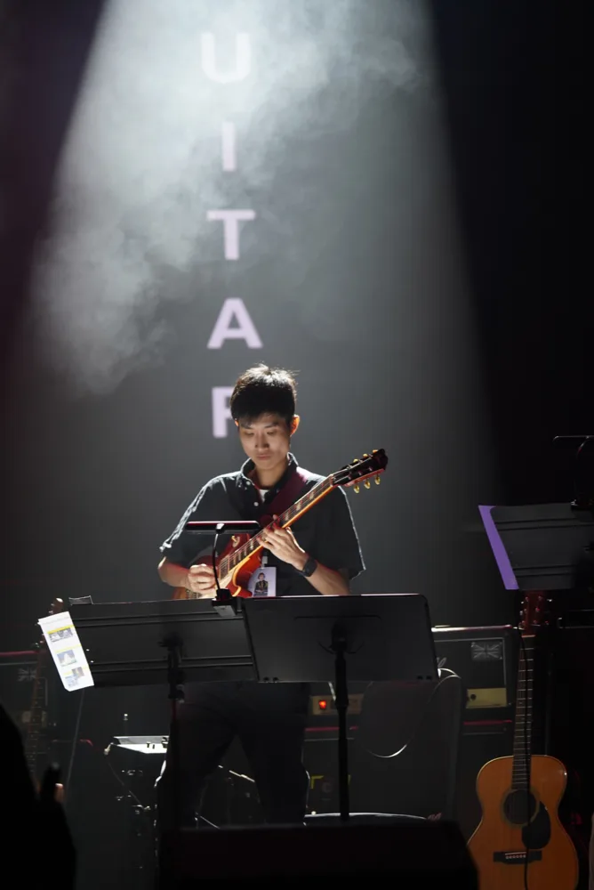 Guitarist playing electric guitar beneath a white spotlight