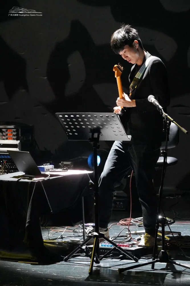 Guitarist performing under a spotlight, with a music stand and effects pedals